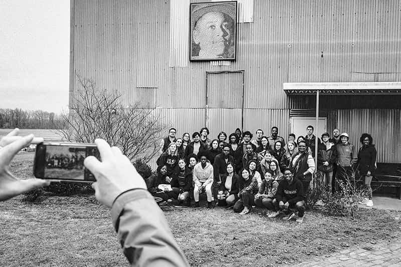 Someone takes a photo with their phone of the class in front of a metal barn.