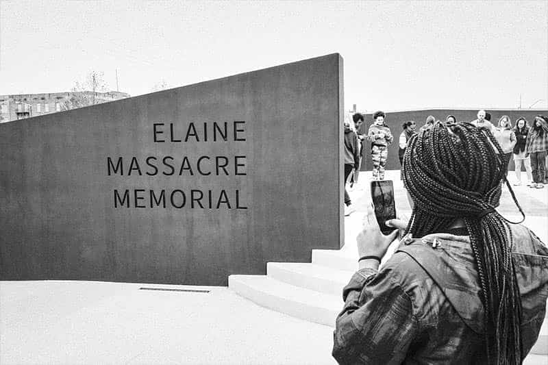 A woman takes a photo of the Elaine Massacre Memorial with her phone.