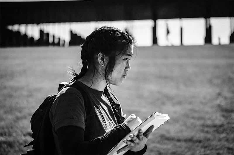 A student holding a notepad and looking off in the distance.