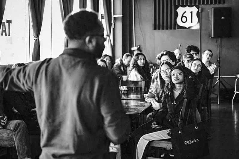 A man speaks to a group of students sitting down at a table.