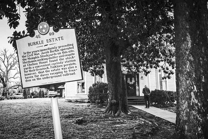 A sign in the foreground and a house and man in the background.