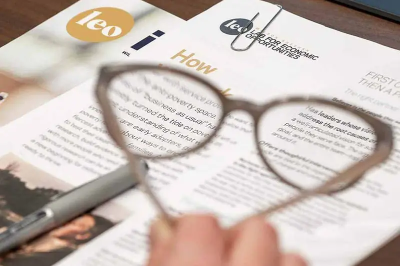 Papers and booklets on a desk and glasses in blurred in the foreground.