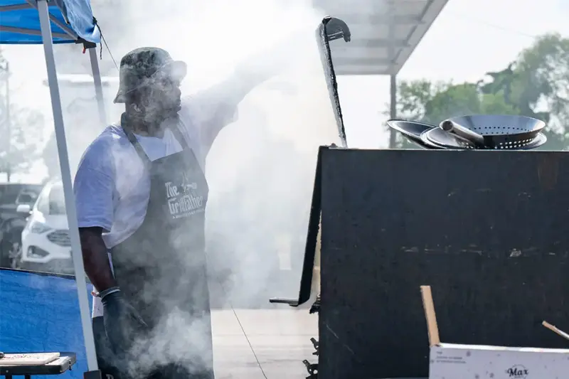 Entrepreneur Raymond Barbour stands in front of his port-a-pit grill while smoke envelopes his face.
