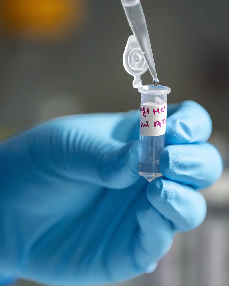 A gloved hand holding a sample of fentanyl in a test tube. 